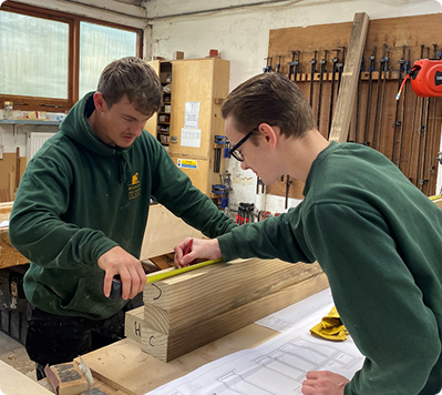 Two apprentices measuring timber in workshop