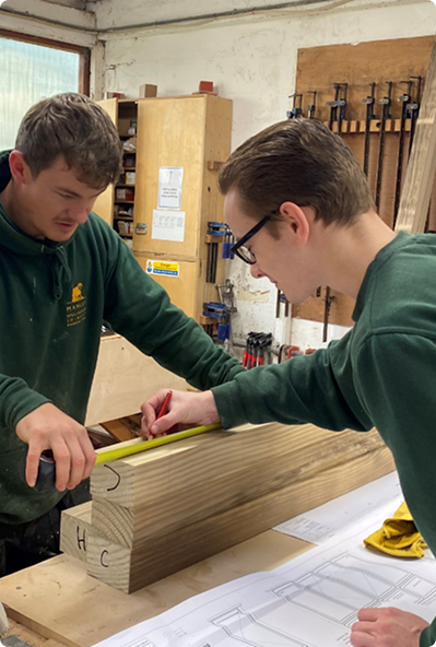 Two apprentices measuring timber in workshop